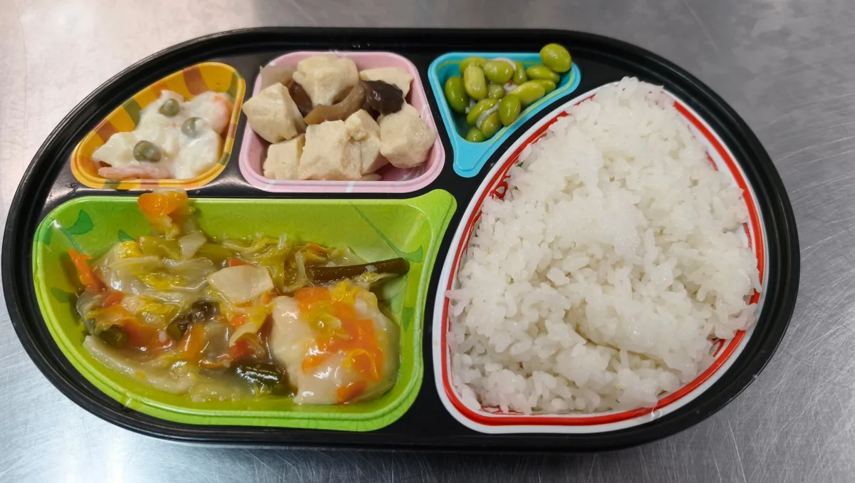 黒い楕円の容器に、ご飯と4品のおかず（あんかけ、煮物、サラダ、枝豆）が入ったお弁当